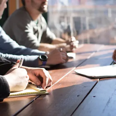 close up view of hands taking notes for a meeting around a wooden table