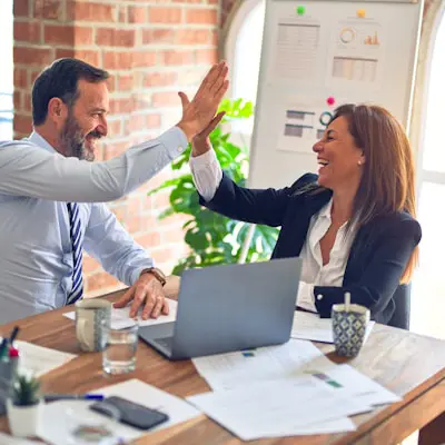 two business professionals high-fiving at a table with a laptop and beverages